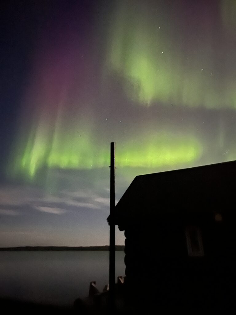 northern lights over a lake with a cabin